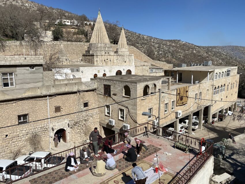 Local men enjoy their lunch together on the rooftops of a nearby home overlooking the entrance road into Lalesh.