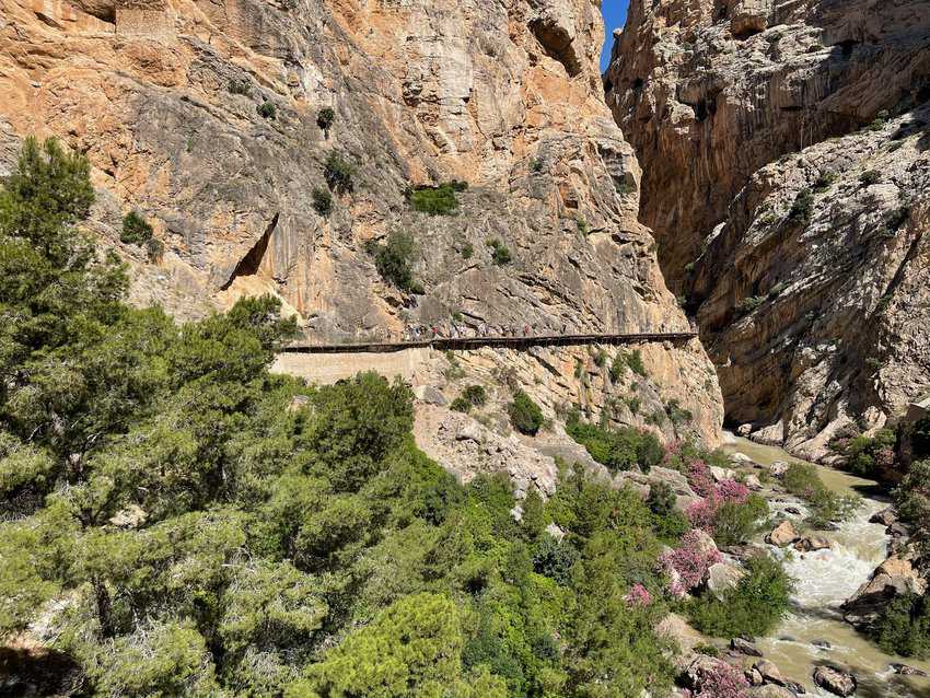 Walkers across the canyon can be seen hiking the narrow wooden trail on the side of the cliff.