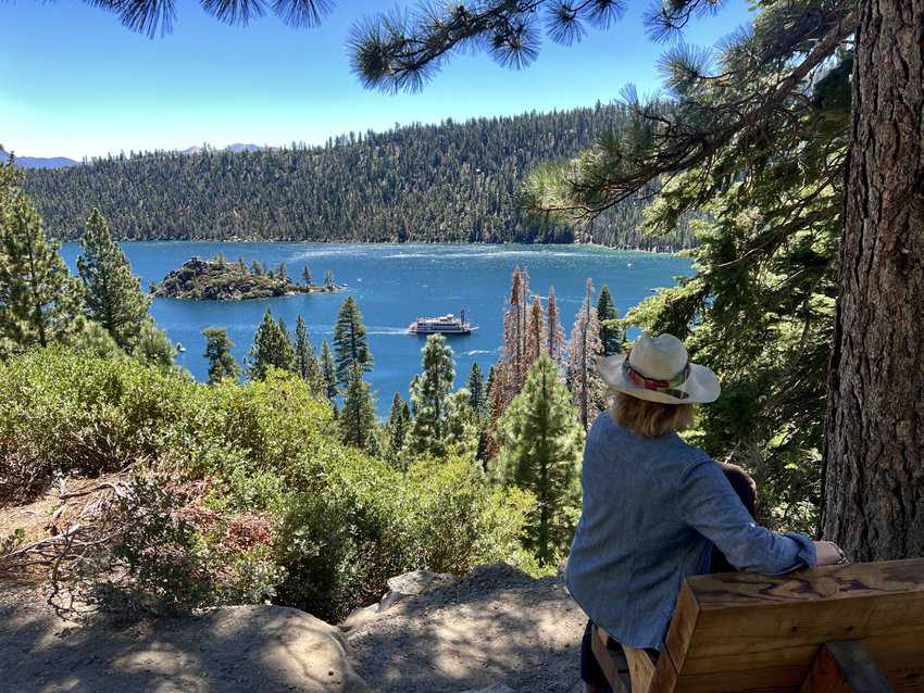 View of Emerald Bay in Lake Tahoe with women on a bench in the foreground and boat on the water. 