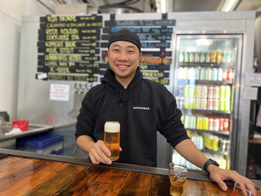 An image of Youngwon Lee, founder of Dokkabier Craft Brewery, holding a beer in his hands in front of the counter at Jack London Square.